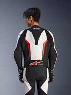 Combinaison en cuir Alpinestars GP Force V2 1 pièce, blanc, noir et rouge fluo, vue de dos sur un modèle masculin, avec bosse aérodynamique, panneaux en cuir perforé et logo Tech-Air Ready dans le bas du dos, équipement de course professionnel avec gants noirs et blancs