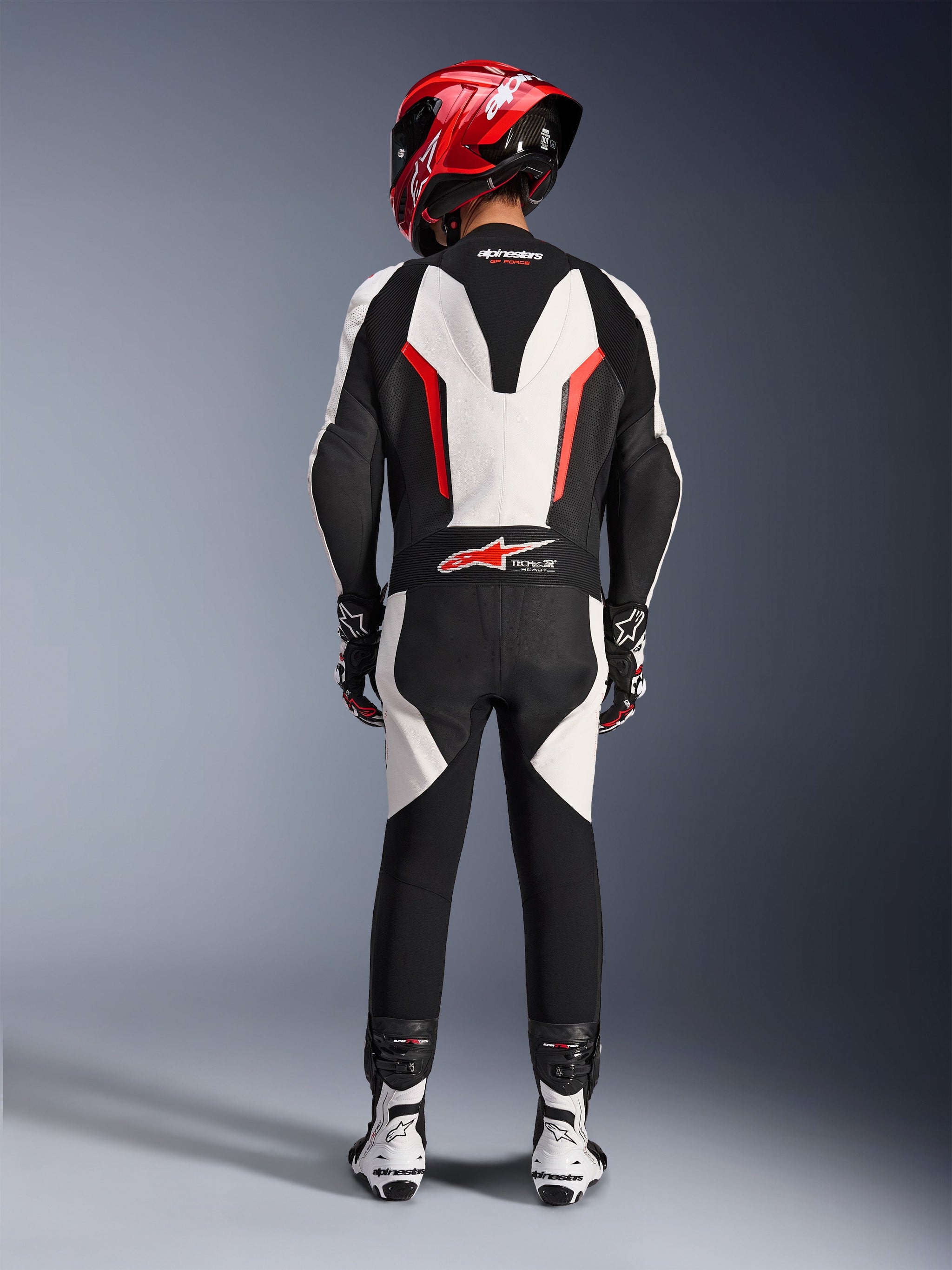 Combinaison en cuir Alpinestars GP Force V2 - 1 pièce, blanc, noir et rouge fluo, vue arrière mettant en évidence la bosse aérodynamique et le logo Tech-Air Ready, portée avec un casque de course rouge et des bottes blanches et noires, conçue pour la performance sur piste