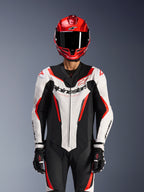 Combinaison en cuir Alpinestars GP Force V2 - 1 pièce, blanc, noir et rouge fluo, portée avec un casque intégral rouge et des gants de course noirs, panneaux en cuir perforé et logo Alpinestars sur la poitrine, équipement de performance professionnel pour la course moto
