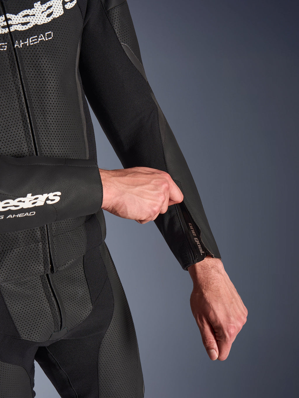 Alpinestars GP Force V2 Leather Suit 2-Piece, combinaison de moto en cuir noir, gros plan sur l'ajustement de l'ouverture zippée de l'avant-bras, avec des panneaux en cuir perforé et une construction en tissu extensible.
