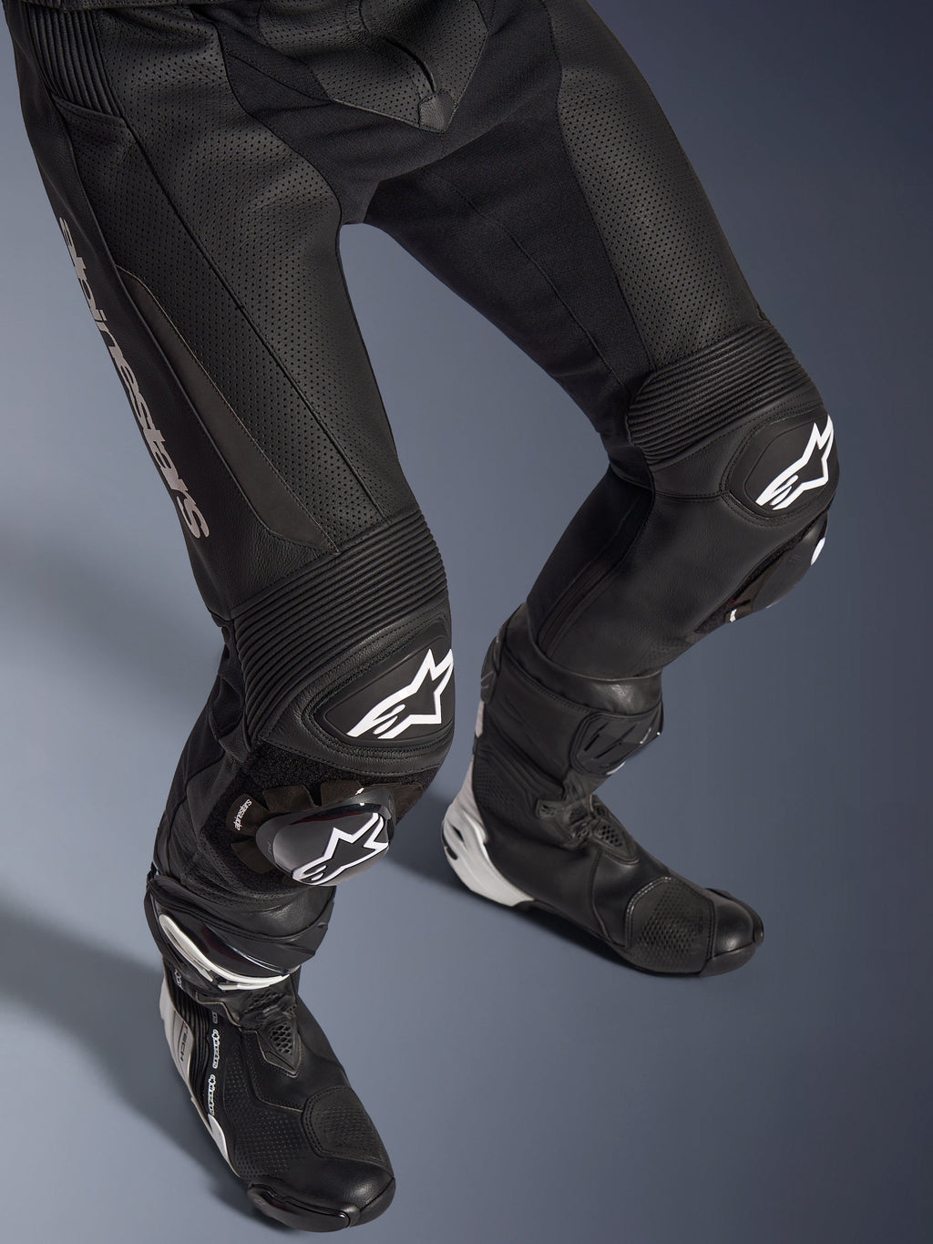 Combinaison en cuir 2 pièces Alpinestars GP Force V2, gros plan du bas du corps avec pantalon et bottes de course, noir avec logos blancs, construction en cuir perforé, panneaux extensibles en accordéon aux genoux et sliders de protection, équipement de conduite sportive professionnelle