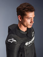Combinaison en cuir Alpinestars GP Force V2, 2 pièces, noire, portée par un mannequin, présentant l'épaule avec logo Astar blanc, le marquage sur la poitrine, les panneaux en cuir perforé et la bosse aérodynamique, équipement de moto haute performance pour la course