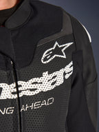 Combinaison en cuir 2 pièces Alpinestars GP Force V2, combinaison de moto de course/sport, noire, gros plan de la poitrine en cuir perforé avec logo et lettrage Alpinestars blancs, soulignant les perforations de ventilation et la construction texturée.
