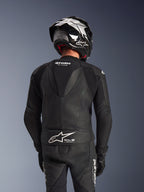 Combinaison en cuir Alpinestars GP Force V2 2 pièces, noire, vue arrière du pilote montrant la bosse aérodynamique, les panneaux en cuir perforé et les zones extensibles en accordéon sur les épaules, avec marquage Tech-Air Ready dans le bas du dos, portée avec un casque de course et des gants assortis.