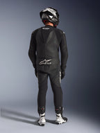 Combinaison en cuir 2 pièces Alpinestars GP Force V2 en noir, vue arrière complète montrant la bosse aérodynamique et le marquage Tech-Air Ready, associée à un casque noir et blanc et des bottes de course blanches pour une performance professionnelle sur circuit