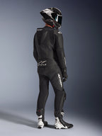 Combinaison en cuir 2 pièces Alpinestars GP Force V2, noire, vue arrière d'un pilote portant un équipement de course complet, avec bosse aérodynamique, logos blancs et cuir perforé, associée à un casque en fibre de carbone et des bottes de course noires et blanches