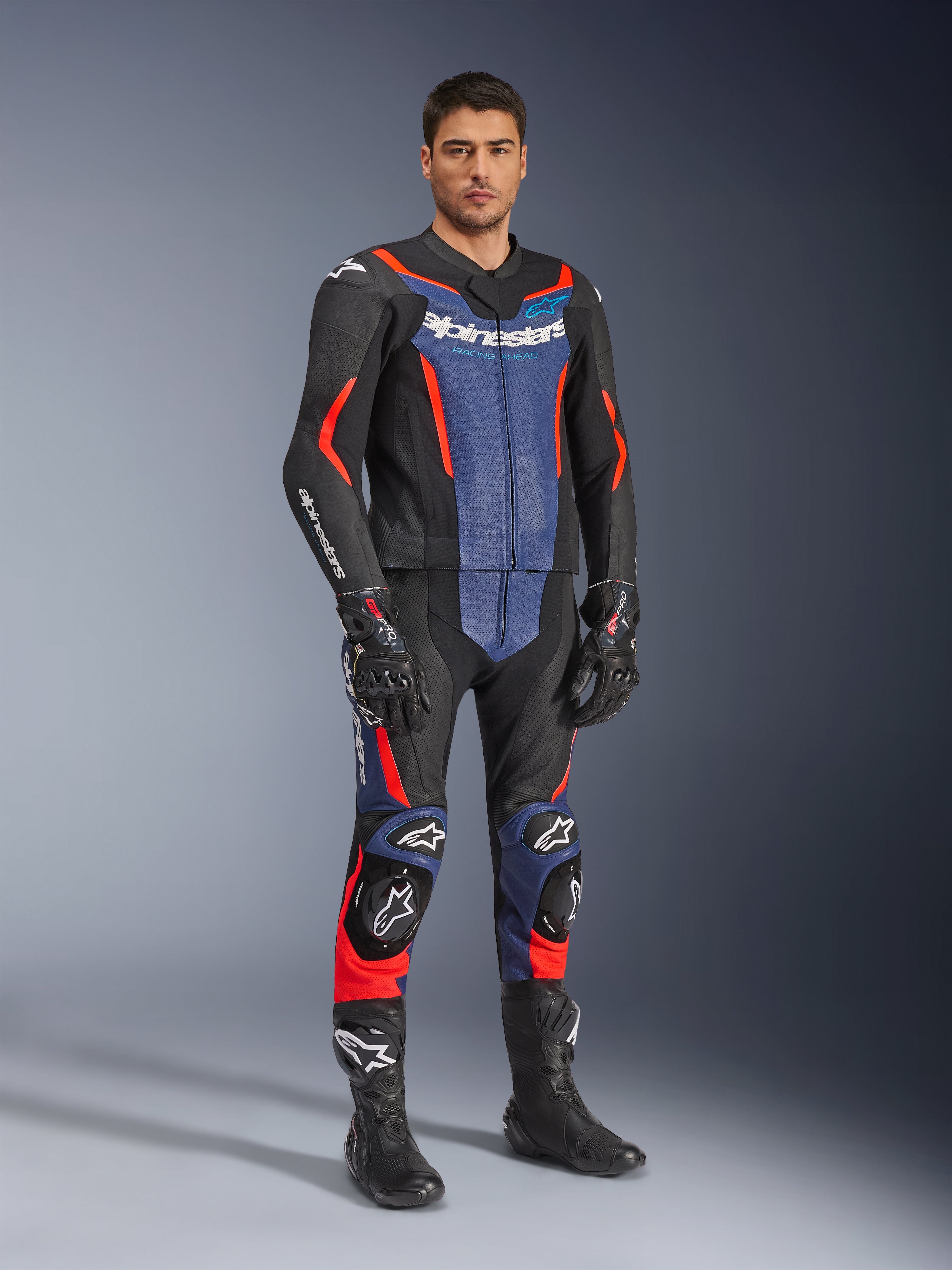 Combinaison en cuir 2 pièces Alpinestars GP Force V2, combinaison de moto en cuir, noir, bleu et rouge fluo, portée avec des gants et des bottes de course noirs assortis, avec panneaux perforés et sliders de protection, design aérodynamique pour la conduite sportive