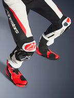Combinaison en cuir 2 pièces Alpinestars Stella GP-R7 pour femme, bas des jambes et bottes de course, noir, blanc et rouge fluo, avec cuir perforé, logo Alpinestars imposant sur la cuisse, panneaux extensibles en accordéon et sliders de genoux rouges et blancs avec bottes techniques assorties rouges et noires.