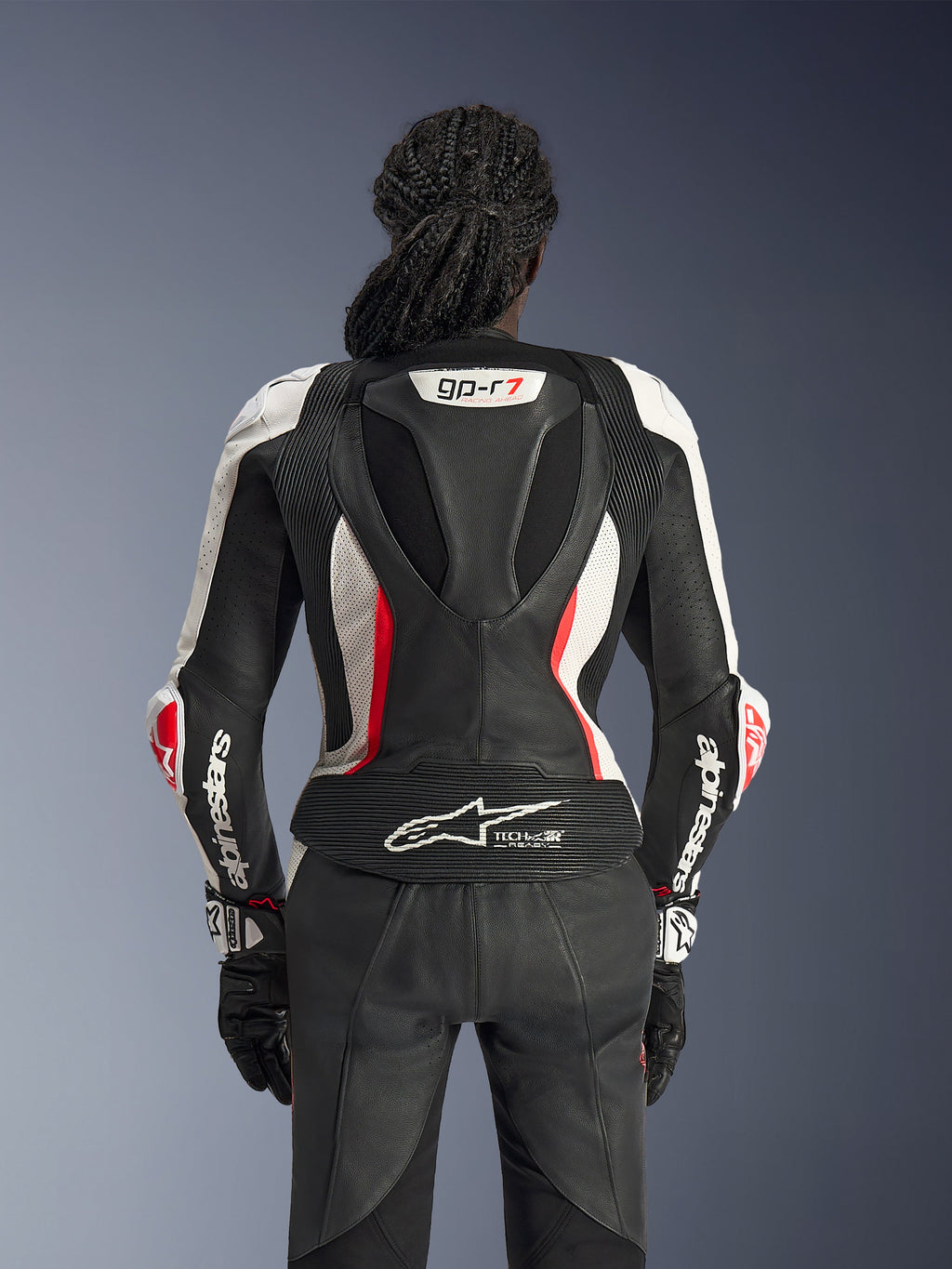 Vue arrière de la combinaison en cuir 2 pièces Alpinestars Stella GP-R7 en noir, blanc et rouge fluo, avec bosse aérodynamique arborant le logo GP-R7, panneaux en cuir perforé, zones extensibles en accordéon et logo Tech-Air® Ready sur le bas du dos.