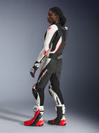 Femme portant la combinaison en cuir 2 pièces Alpinestars Stella GP-R7, noir, blanc et rouge fluo, vue de profil montrant la bosse dorsale aérodynamique et les sliders de genou, associée à des gants et bottes de course Alpinestars assortis, équipement professionnel de piste