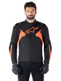 Alpinestars T-Jaws V4 Waterproof Jacket, veste de moto sport, noir et rouge fluo, avec des accents néon et un logo étoile proéminent sur la poitrine, portée par un modèle masculin avec des gants de moto noirs, design textile épuré inspiré de la course