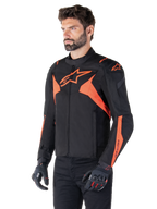 Veste imperméable Alpinestars T-Jaws V4, Noir et Rouge Fluo, veste de moto sport portée par un mannequin homme, arborant des logos d'étoiles orange sur la poitrine et les épaules, associée à des gants et un pantalon noirs