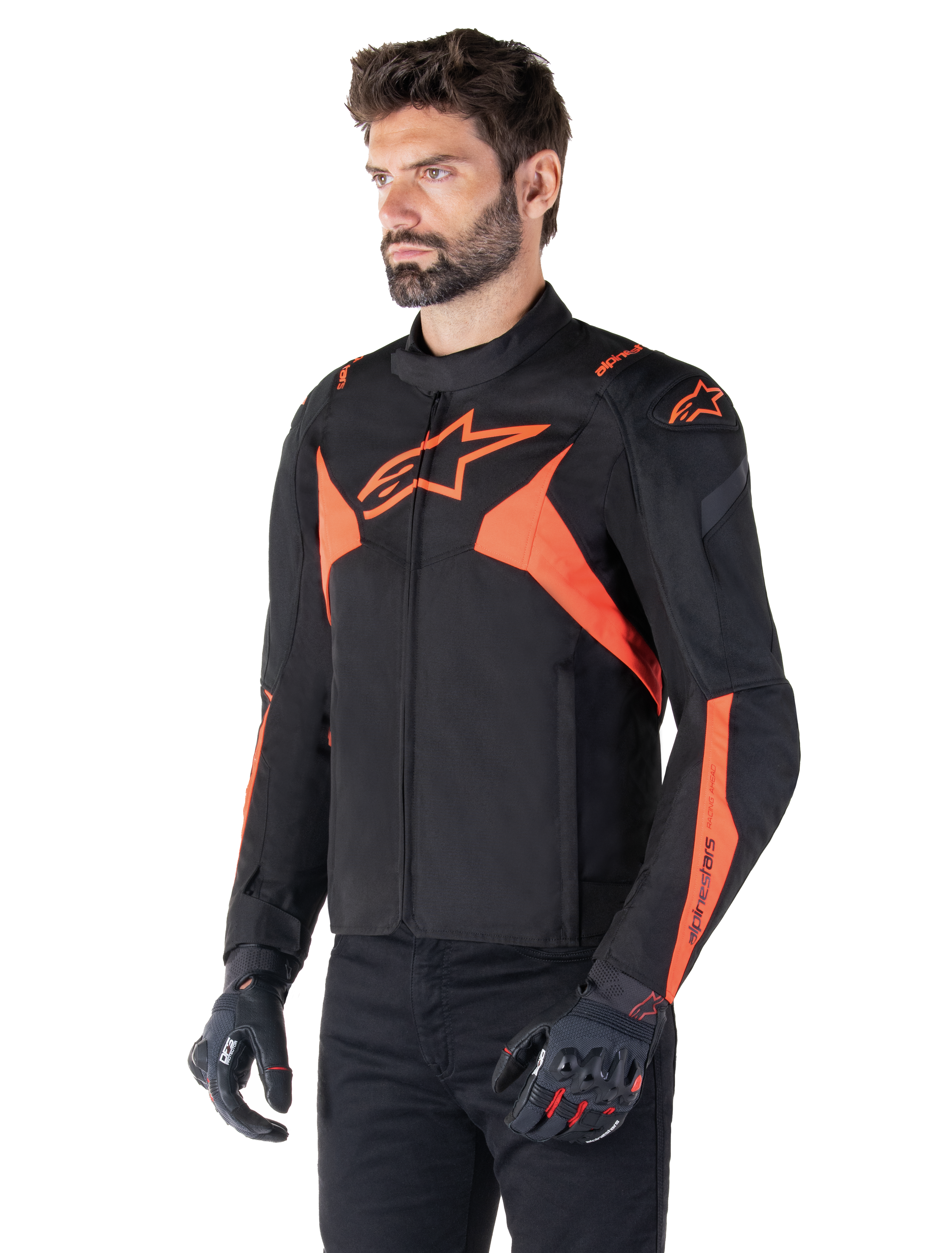Veste imperméable Alpinestars T-Jaws V4, Noir et Rouge Fluo, veste de moto sport portée par un mannequin homme, arborant des logos d'étoiles orange sur la poitrine et les épaules, associée à des gants et un pantalon noirs
