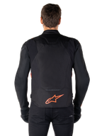 Veste imperméable Alpinestars T-Jaws V4, vue arrière, noir et rouge fluo, arborant un logo Alpinestars rouge en bas du dos, construction en textile technique, portée avec un pantalon et des gants noirs pour un look de pilotage sportif complet