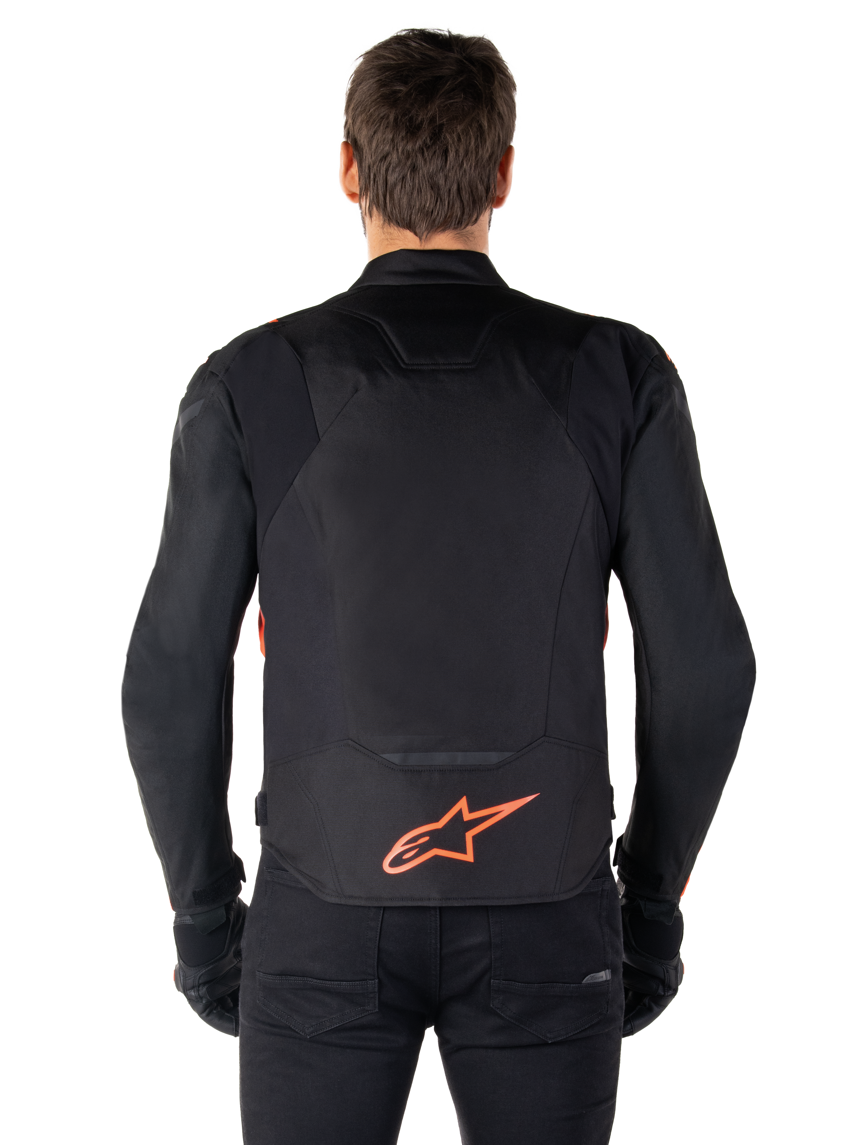Veste imperméable Alpinestars T-Jaws V4, vue arrière, noir et rouge fluo, arborant un logo Alpinestars rouge en bas du dos, construction en textile technique, portée avec un pantalon et des gants noirs pour un look de pilotage sportif complet