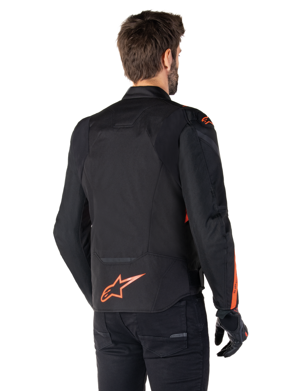 Modèle masculin portant la veste imperméable Alpinestars T-Jaws V4 vue de dos, noir avec des accents rouge fluo, présentant un logo rouge fluo au bas du dos et des détails sur les épaules et les manches, équipement de moto sportif.