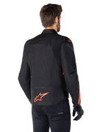 Modèle masculin portant la veste imperméable Alpinestars T-Jaws V4 vue de dos, noir avec des accents rouge fluo, présentant un logo rouge fluo au bas du dos et des détails sur les épaules et les manches, équipement de moto sportif.