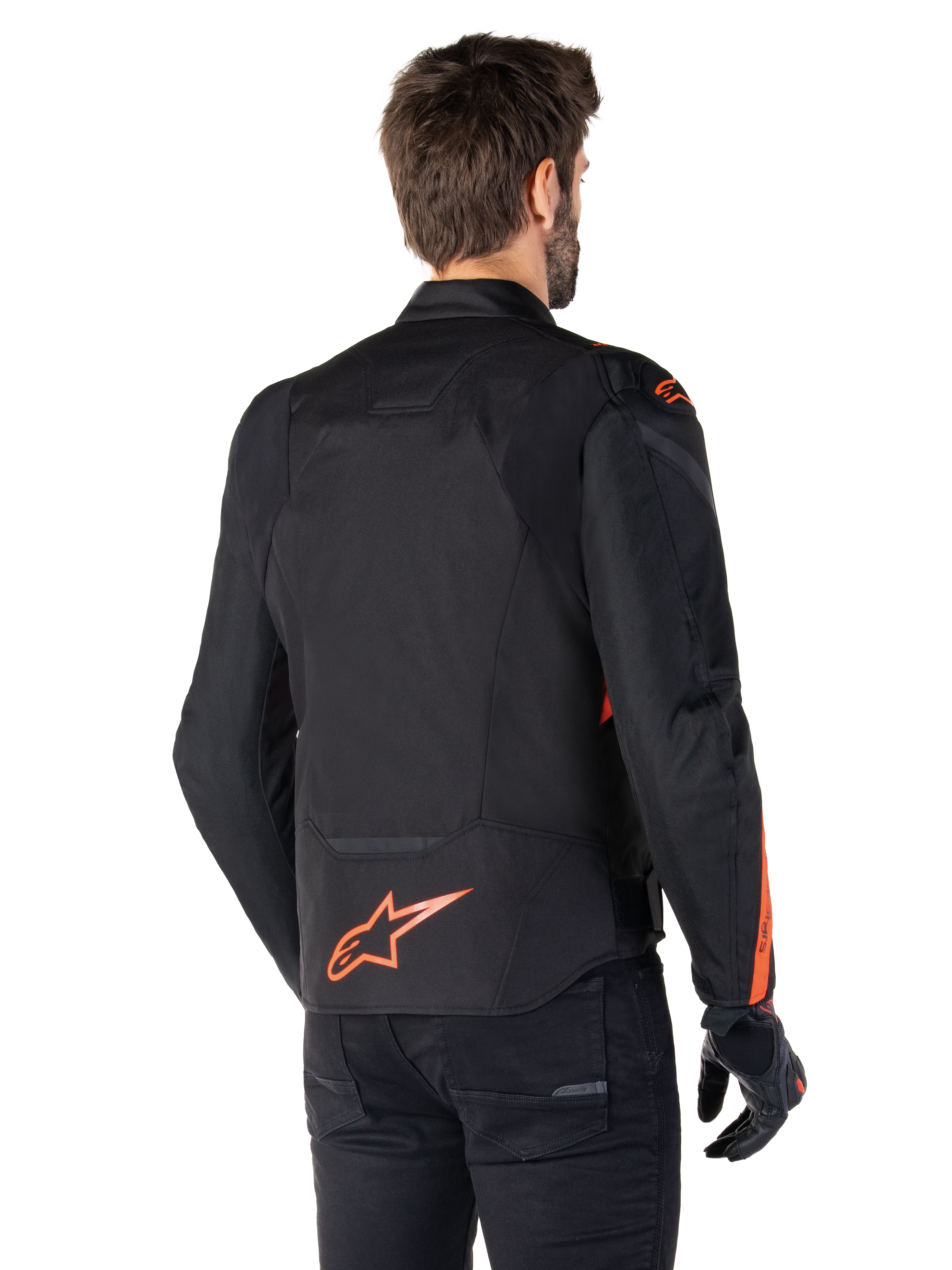 Modèle masculin portant la veste imperméable Alpinestars T-Jaws V4 vue de dos, noir avec des accents rouge fluo, présentant un logo rouge fluo au bas du dos et des détails sur les épaules et les manches, équipement de moto sportif.