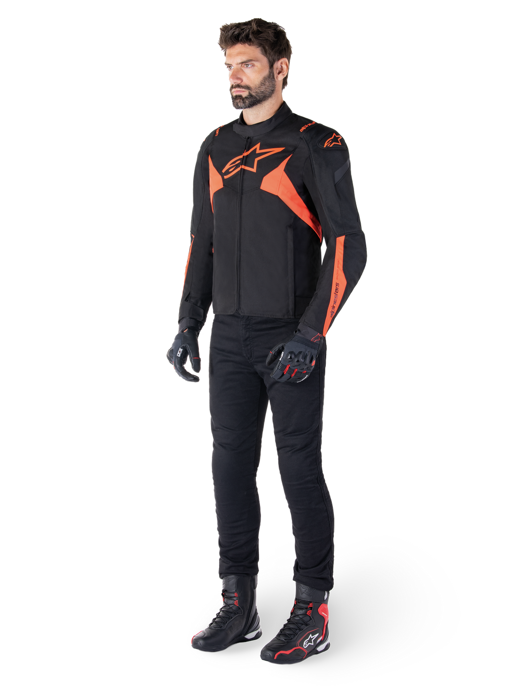 Veste imperméable Alpinestars T-Jaws V4, noir et rouge fluo, portée par un mannequin homme avec pantalon, gants et bottes noirs, avec des accents orange vif et le logo Alpinestars, design sportif pour la conduite de moto