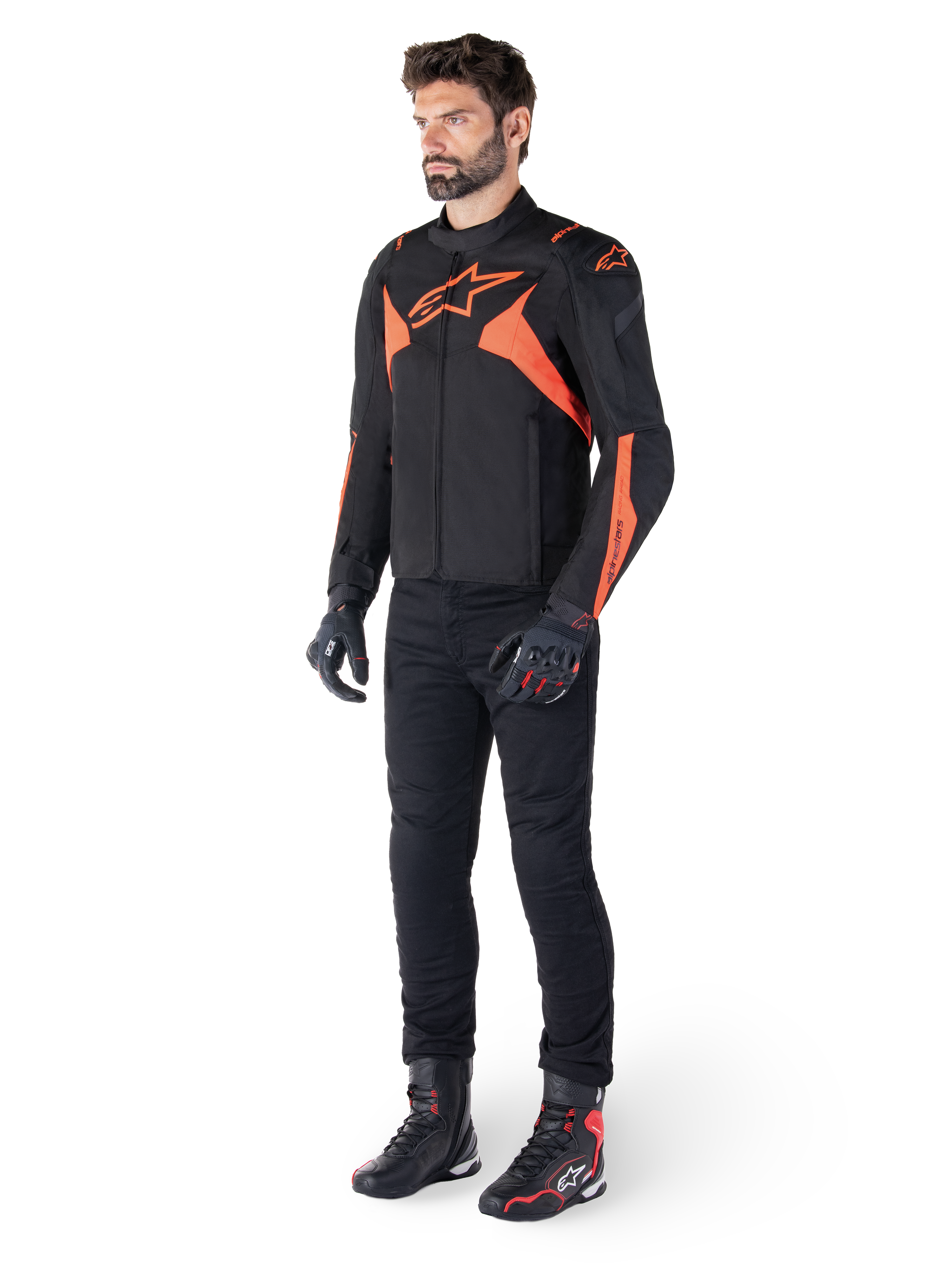 Veste imperméable Alpinestars T-Jaws V4, noir et rouge fluo, portée par un mannequin homme avec pantalon, gants et bottes noirs, avec des accents orange vif et le logo Alpinestars, design sportif pour la conduite de moto