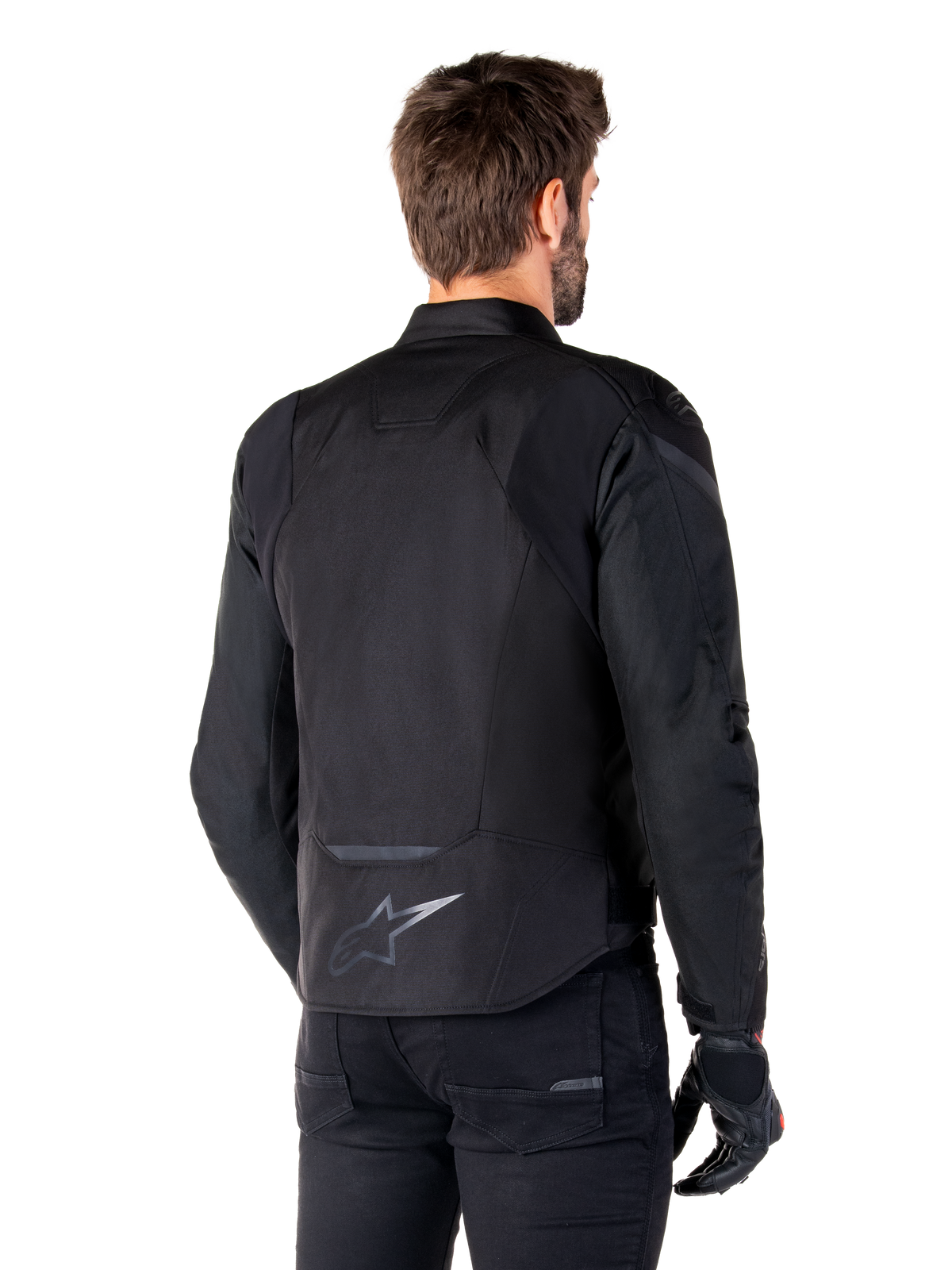 Veste imperméable Alpinestars T-Jaws V4, noire, vue de dos sur mannequin, dotée d'un logo Alpinestars réfléchissant dans le bas du dos, dos allongé pour une meilleure protection, design textile sportif avec des panneaux ton sur ton, portée avec des gants de moto noirs.