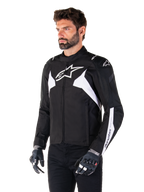 Veste imperméable Alpinestars T-Jaws V4, noir et blanc, portée par un mannequin avec des gants de moto, arborant des logos et des accents Alpinestars blancs proéminents, veste de moto en textile à coupe sport pour la route