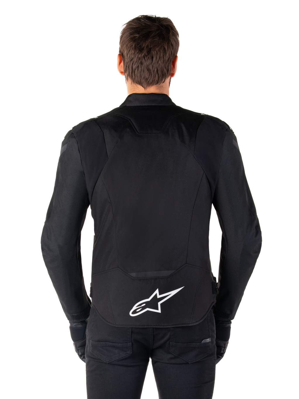 Alpinestars T-Jaws V4 Waterproof Jacket, veste de moto noire vue de dos, arborant un logo Alpinestars blanc sur le bas du dos, dos rallongé pour une meilleure protection, portée par un mannequin avec pantalon et gants noirs, design textile sport épuré