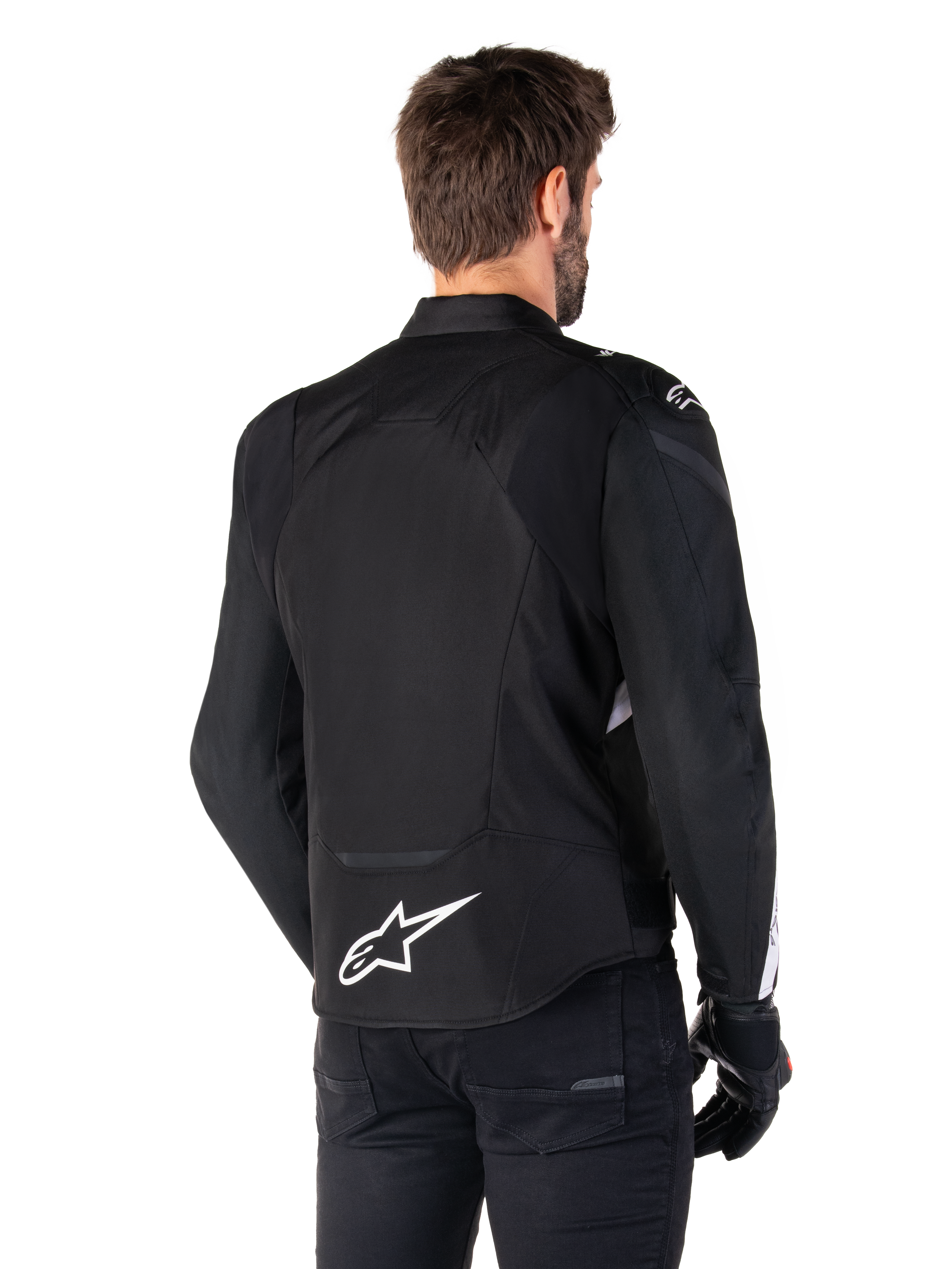 Veste étanche Alpinestars T-Jaws V4, noir et blanc, vue arrière, veste de moto sport en textile avec logo blanc sur le bas du dos, portée avec des gants et un pantalon noirs, présentant une silhouette à coupe sport révisée