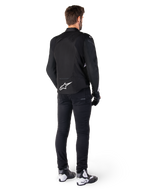 Veste imperméable Alpinestars T-Jaws V4, noir et blanc, vue arrière montrant le logo étoile blanc sur le bas du dos, portée par un mannequin avec un pantalon de moto noir, des gants noirs et des bottes de moto blanches et noires