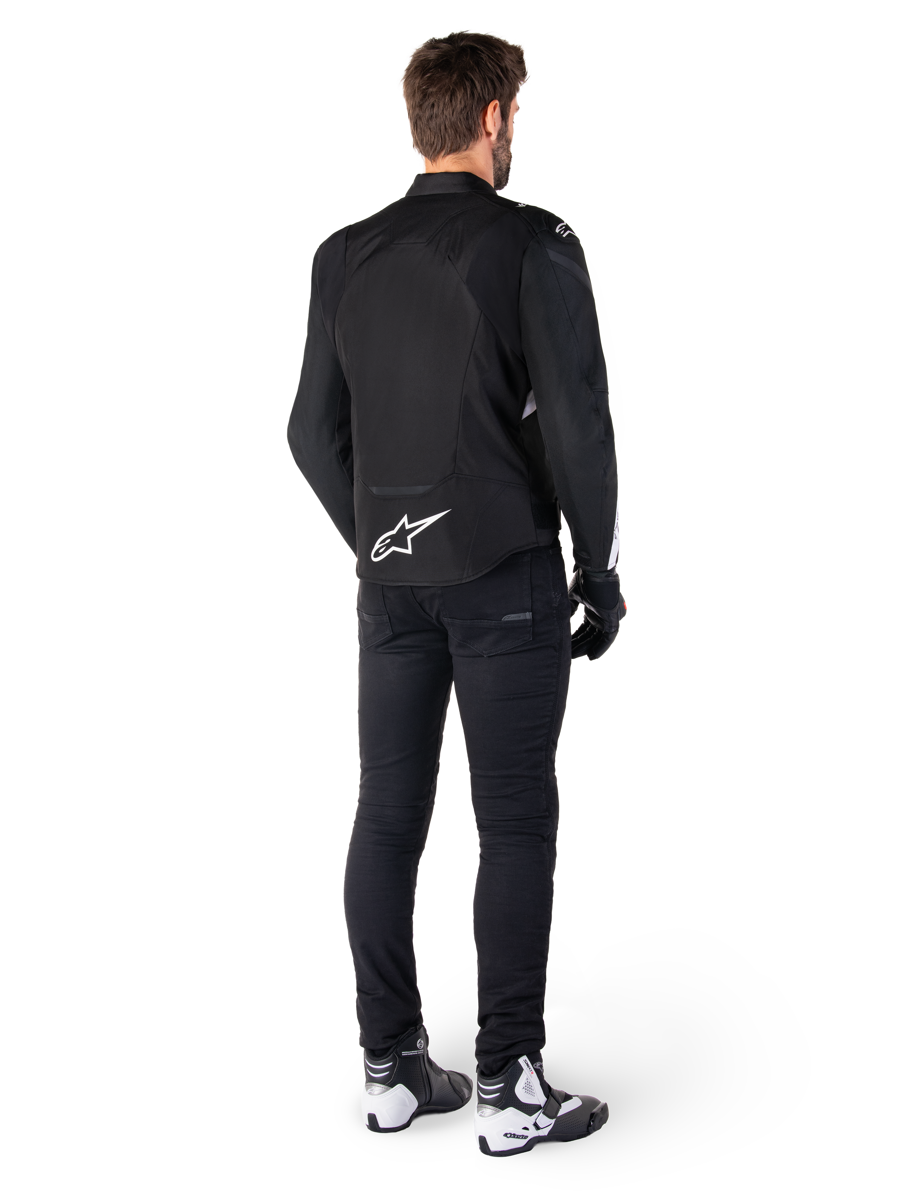 Veste imperméable Alpinestars T-Jaws V4, noir et blanc, vue arrière montrant le logo étoile blanc sur le bas du dos, portée par un mannequin avec un pantalon de moto noir, des gants noirs et des bottes de moto blanches et noires