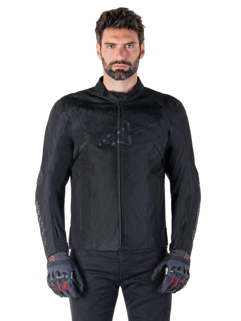 Alpinestars T-SPS V2 Waterproof Jacket, veste de moto textile noire, portée par un motard avec des gants noirs et rouges, dotée d'un col montant, d'une fermeture éclair frontale et d'un logo discret sur la poitrine, protection imperméable pour la conduite sportive et urbaine