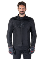 Alpinestars T-SPS V2 Waterproof Jacket, veste de moto textile noire, portée par un motard avec des gants noirs et rouges, dotée d'un col montant, d'une fermeture éclair frontale et d'un logo discret sur la poitrine, protection imperméable pour la conduite sportive et urbaine