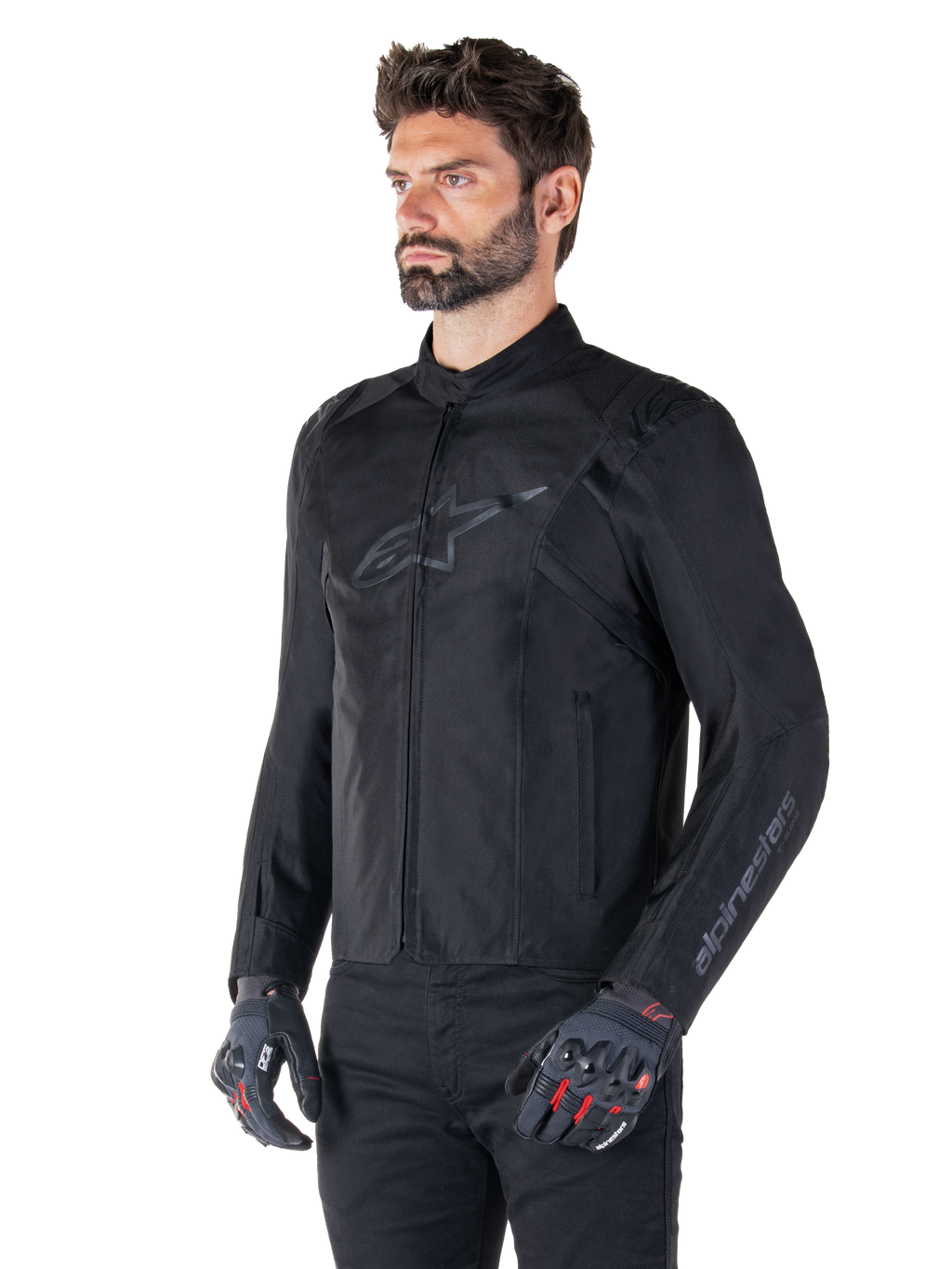 Veste Alpinestars T-SPS V2 Waterproof, noir, portée par un mannequin avec un pantalon noir et des gants de moto gris avec accents rouges, dotée d'un logo discret sur la poitrine et d'un marquage sur la manche, veste textile à coupe sport pour la route.