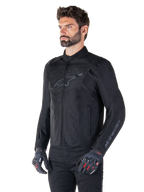Veste Alpinestars T-SPS V2 Waterproof, noir, portée par un mannequin avec un pantalon noir et des gants de moto gris avec accents rouges, dotée d'un logo discret sur la poitrine et d'un marquage sur la manche, veste textile à coupe sport pour la route.