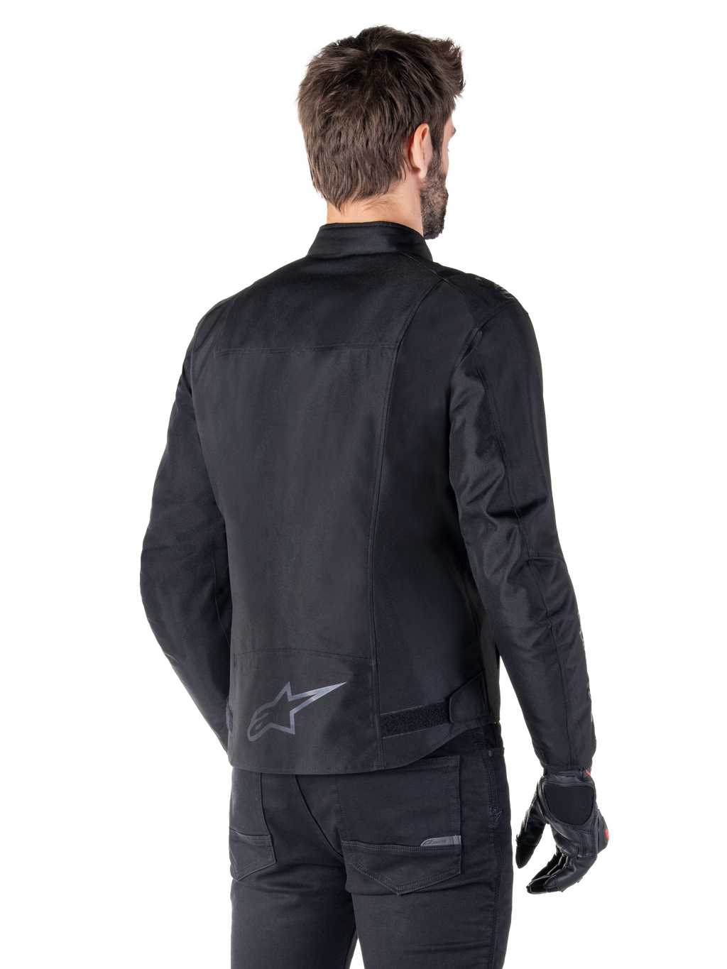 Veste imperméable Alpinestars T-SPS V2, noire, vue arrière sur un mannequin homme, avec un logo étoile réfléchissant dans le bas du dos, un profil arrière allongé et des sangles de réglage à la taille, portée avec un pantalon de moto et des gants noirs