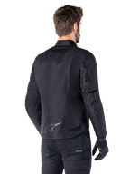 Veste imperméable Alpinestars T-SPS V2, noire, vue arrière sur un mannequin homme, avec un logo étoile réfléchissant dans le bas du dos, un profil arrière allongé et des sangles de réglage à la taille, portée avec un pantalon de moto et des gants noirs