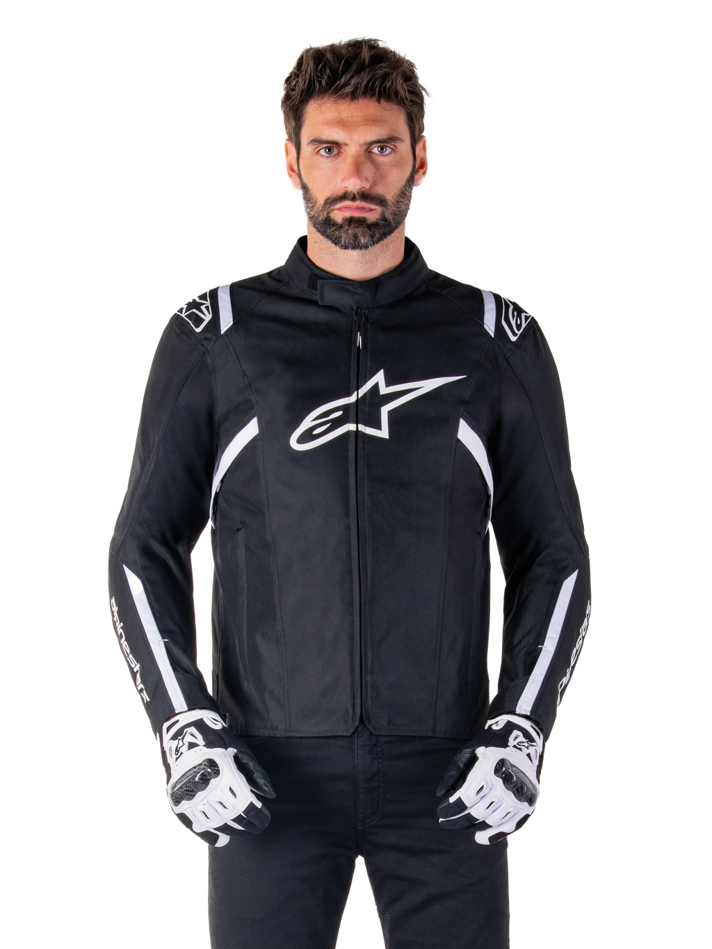 Alpinestars T-SPS V2 Waterproof Jacket en noir et blanc, vue de face sur modèle, veste de moto en textile imperméable avec des bandes blanches sur les épaules et les bras, grand logo Alpinestars blanc sur la poitrine, portée avec des gants de moto protecteurs, silhouette élégante d'inspiration sportive