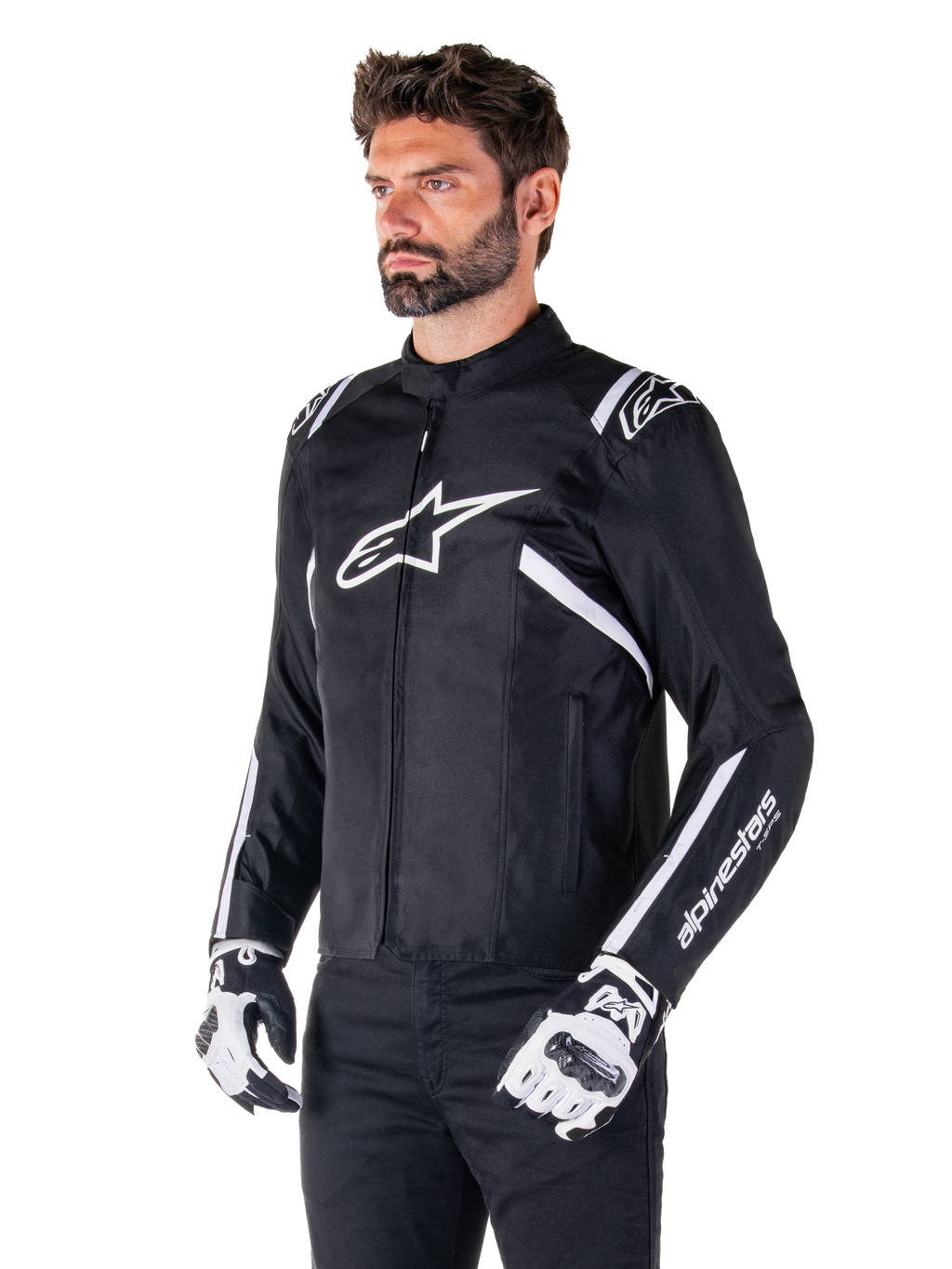 Veste imperméable Alpinestars T-SPS V2, noir et blanc, portée par un mannequin homme avec des gants de moto assortis, veste textile à coupe sport avec logos Alpinestars blancs sur la poitrine et les épaules, marquage « alpinestars T-SPS » sur la manche, équipement de moto élégant inspiré de la course