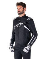 Veste imperméable Alpinestars T-SPS V2, noir et blanc, portée par un mannequin homme avec des gants de moto assortis, veste textile à coupe sport avec logos Alpinestars blancs sur la poitrine et les épaules, marquage « alpinestars T-SPS » sur la manche, équipement de moto élégant inspiré de la course