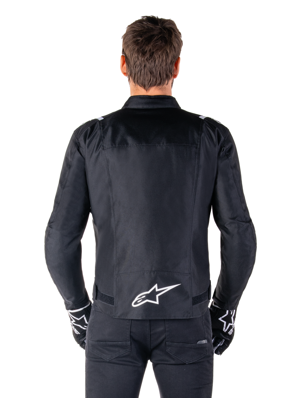 Veste imperméable Alpinestars T-SPS V2, noir et blanc, vue arrière montrant le logo Alpinestars blanc en bas du dos, portée avec un pantalon et des gants noirs, veste de moto en textile à coupe sport
