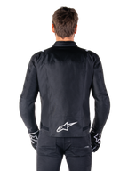 Veste imperméable Alpinestars T-SPS V2, noir et blanc, vue arrière montrant le logo Alpinestars blanc en bas du dos, portée avec un pantalon et des gants noirs, veste de moto en textile à coupe sport