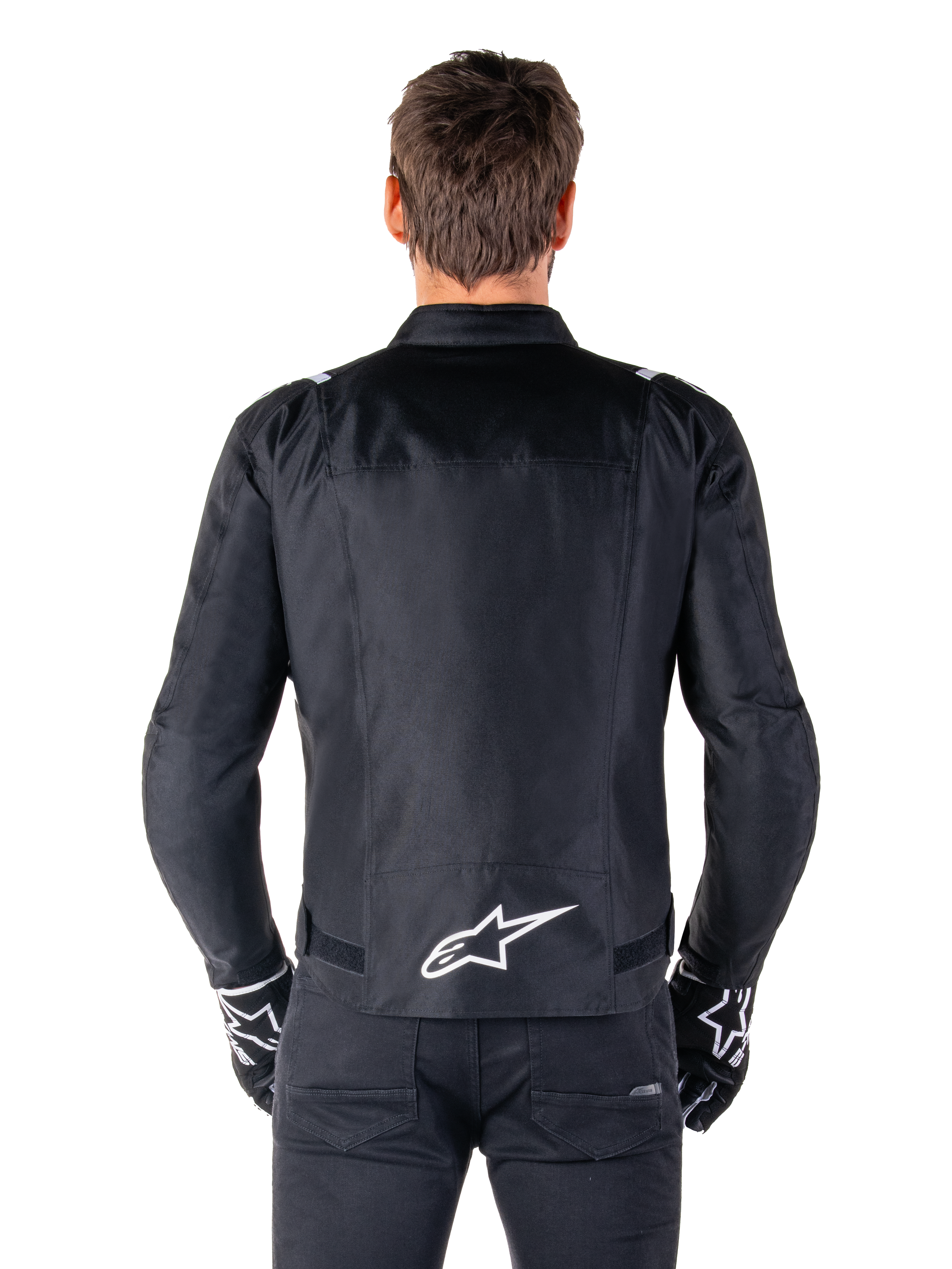 Veste imperméable Alpinestars T-SPS V2, noir et blanc, vue arrière montrant le logo Alpinestars blanc en bas du dos, portée avec un pantalon et des gants noirs, veste de moto en textile à coupe sport