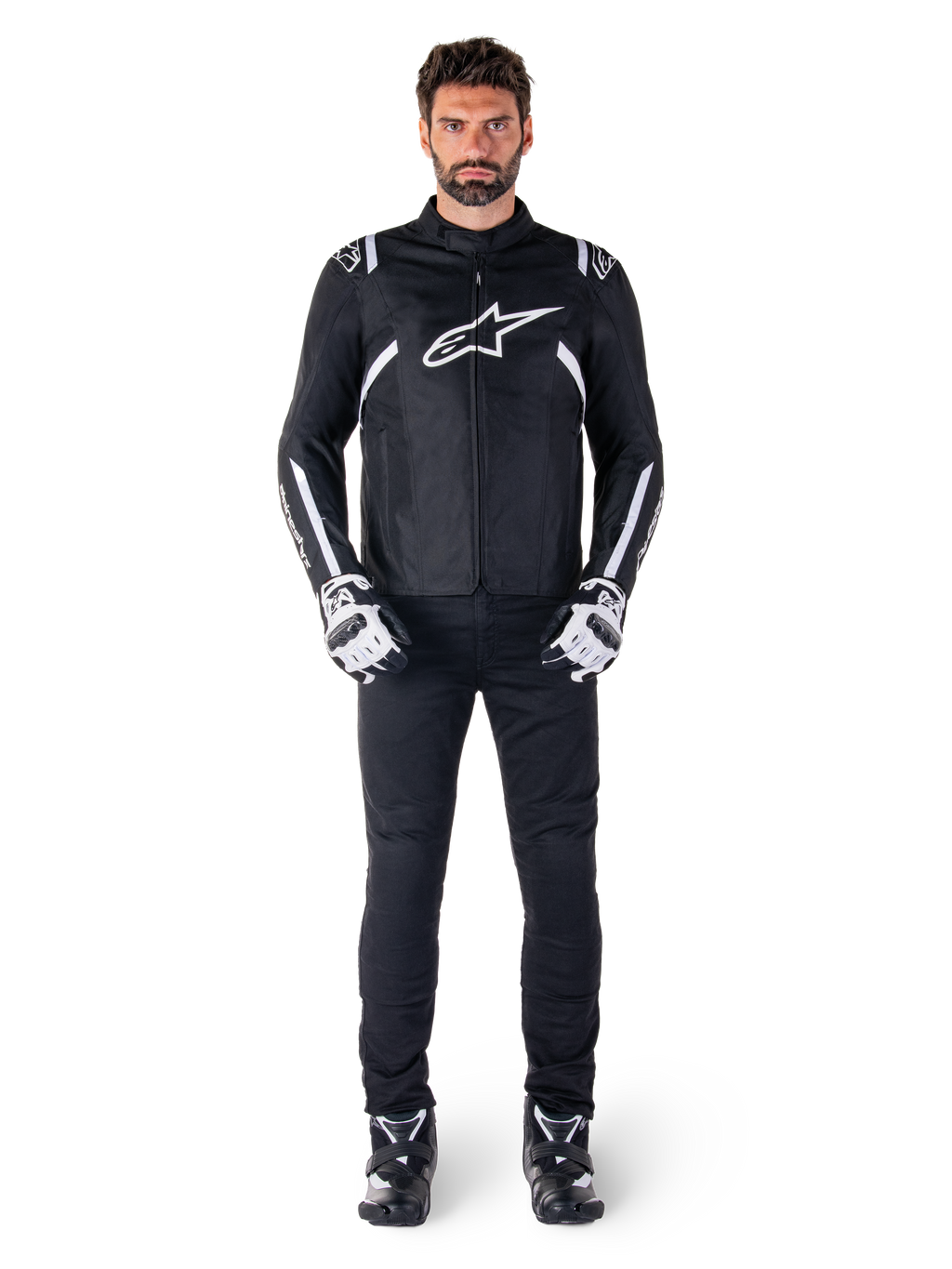 Veste imperméable Alpinestars T-SPS V2, noir et blanc, portée par un mannequin homme avec un pantalon noir et des gants assortis, avec le logo Alpinestars blanc sur la poitrine et des détails sur les manches, silhouette à coupe sport pour la conduite de moto par tous les temps