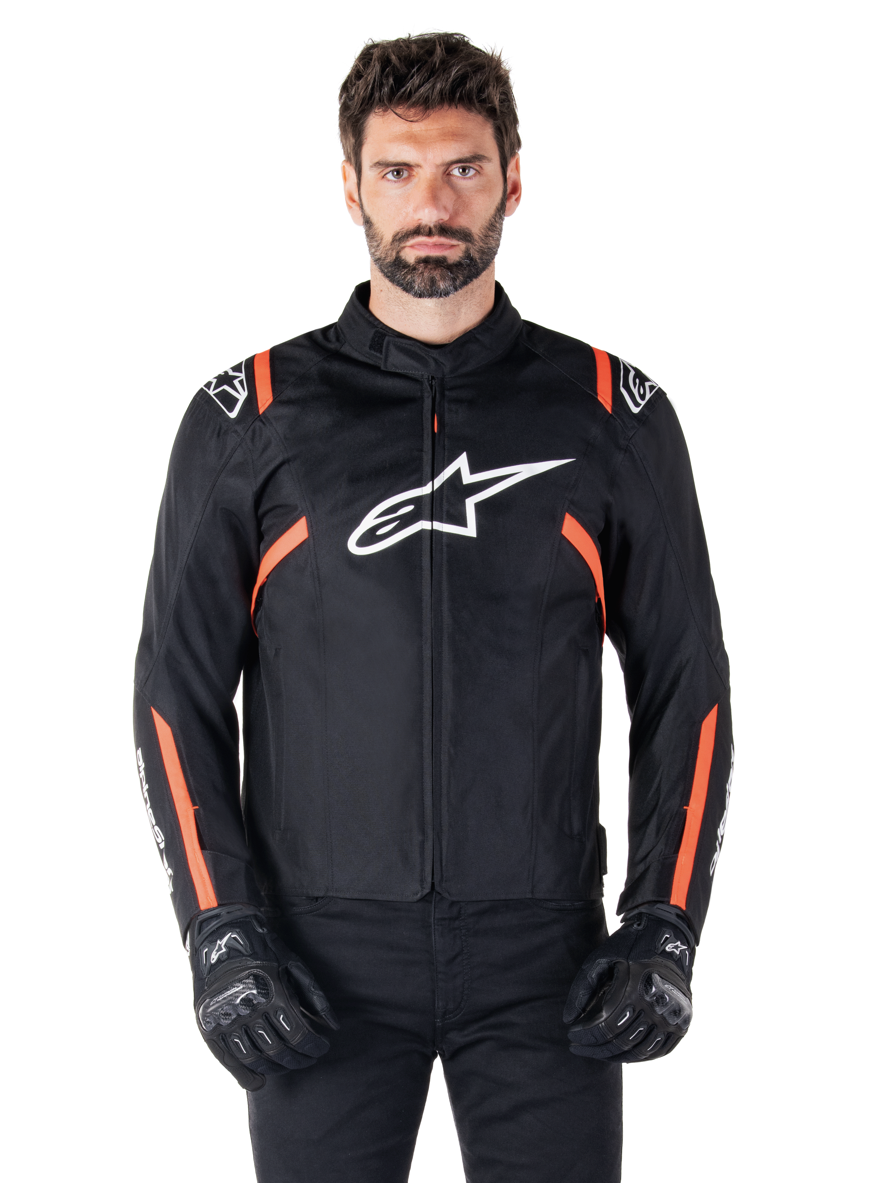 Veste imperméable Alpinestars T-SPS V2, noir, blanc et rouge fluo, portée par un mannequin homme avec des gants de moto noirs, avec un grand logo Alpinestars blanc sur la poitrine et des accents orange vif sur les épaules et les manches.