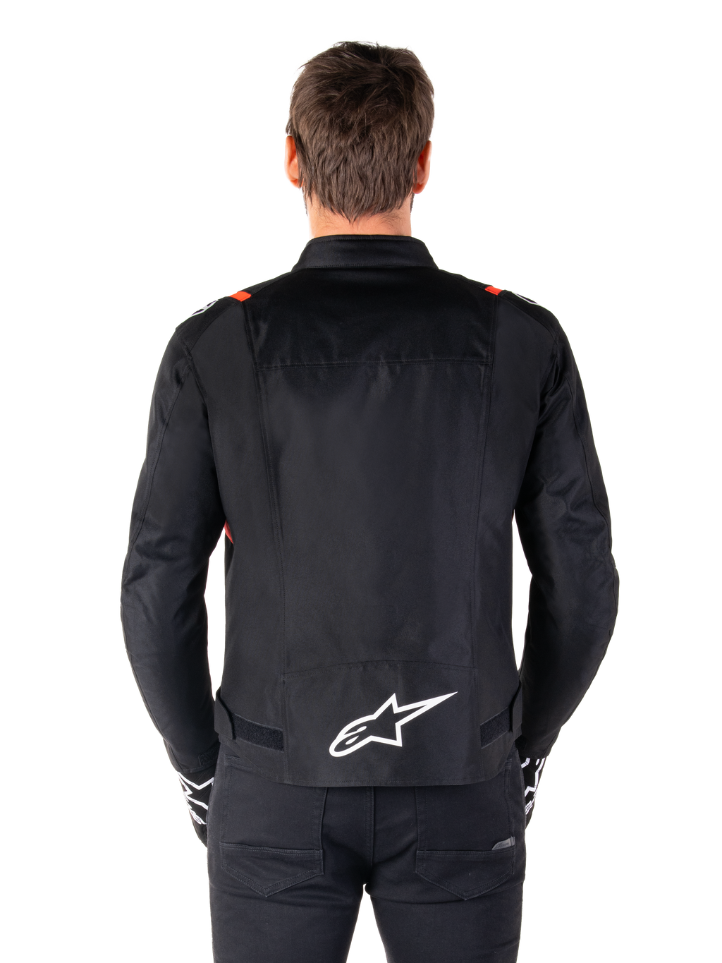Veste imperméable Alpinestars T-SPS V2, noire avec accents blanc et rouge fluo, vue arrière présentant un grand logo Alpinestars blanc en bas du dos, veste de moto en textile coupe sport, portée avec un pantalon et des gants noirs