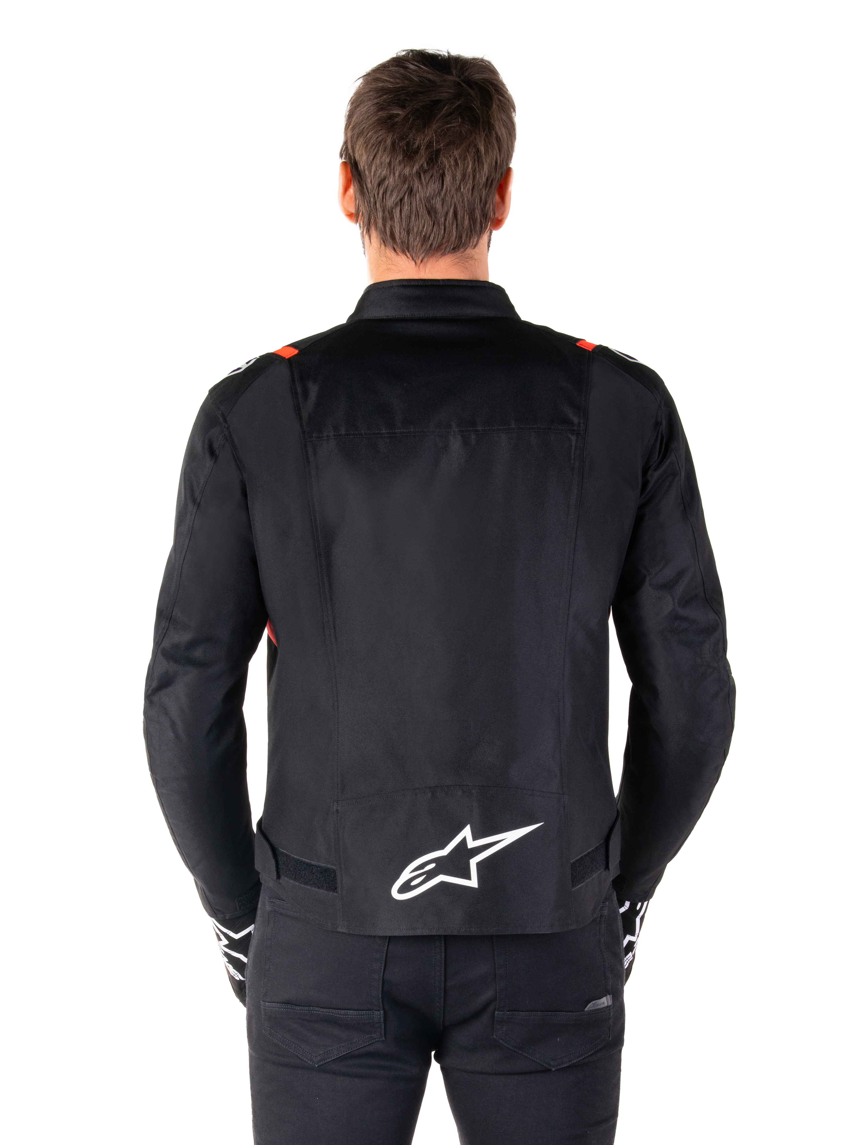 Veste imperméable Alpinestars T-SPS V2, noire avec accents blanc et rouge fluo, vue arrière présentant un grand logo Alpinestars blanc en bas du dos, veste de moto en textile coupe sport, portée avec un pantalon et des gants noirs