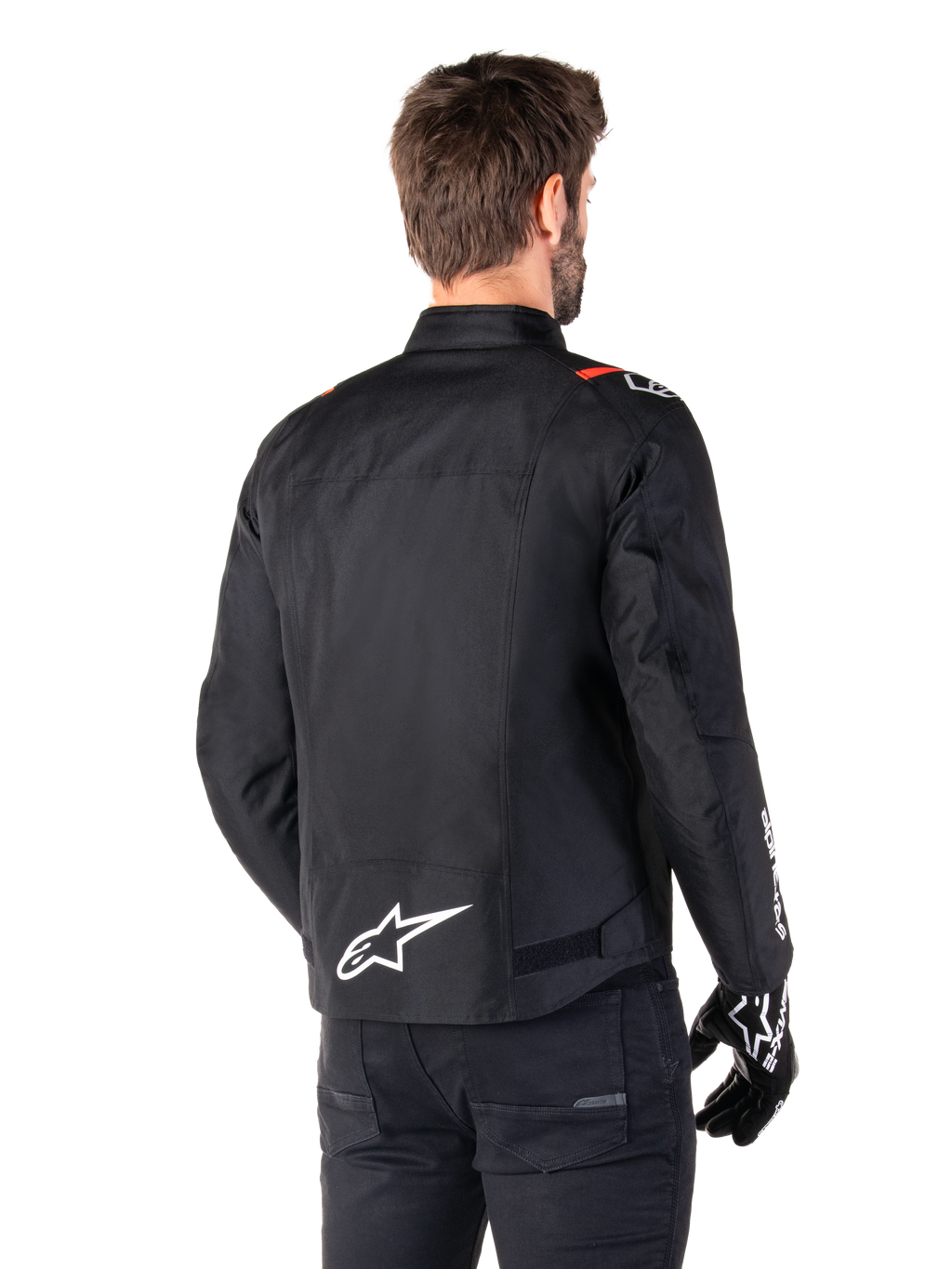 Veste imperméable Alpinestars T-SPS V2, Noir Blanc Rouge Fluo, vue arrière, avec logo Alpinestars blanc en bas du dos et accents rouges sur les épaules, portée avec des gants et un pantalon de moto noirs, veste de moto en textile de style sport.