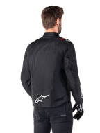 Veste imperméable Alpinestars T-SPS V2, Noir Blanc Rouge Fluo, vue arrière, avec logo Alpinestars blanc en bas du dos et accents rouges sur les épaules, portée avec des gants et un pantalon de moto noirs, veste de moto en textile de style sport.