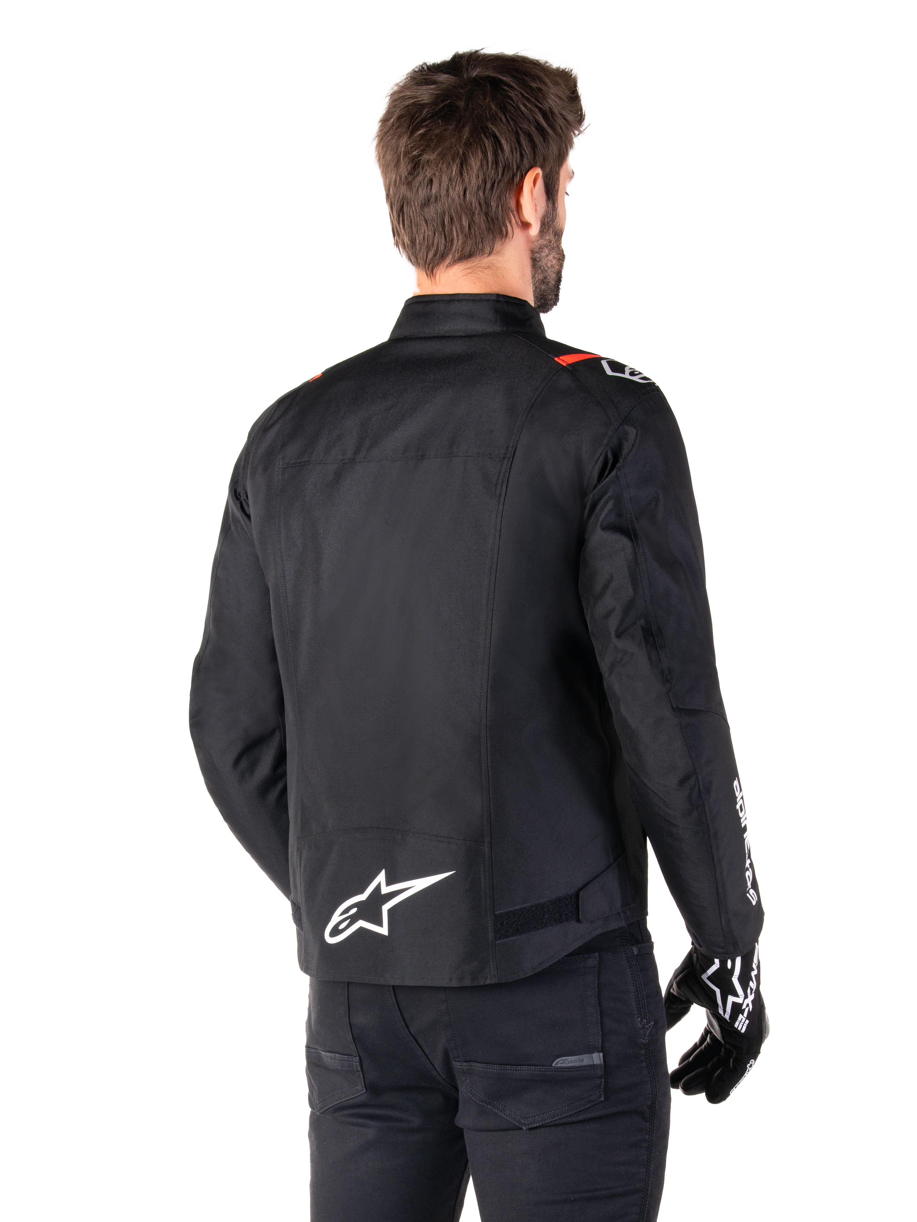 Veste imperméable Alpinestars T-SPS V2, Noir Blanc Rouge Fluo, vue arrière, avec logo Alpinestars blanc en bas du dos et accents rouges sur les épaules, portée avec des gants et un pantalon de moto noirs, veste de moto en textile de style sport.