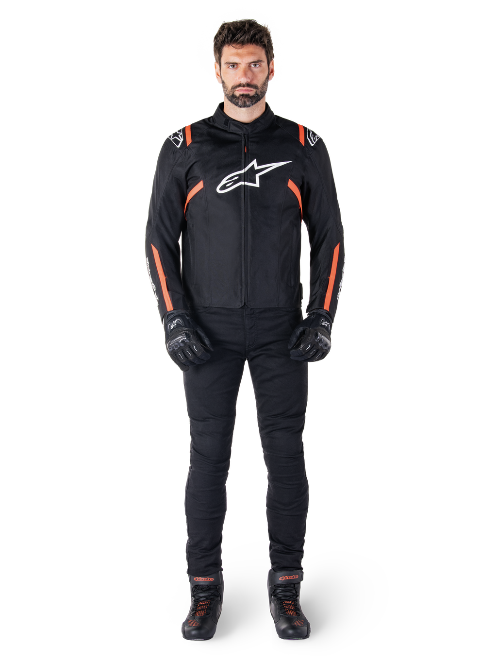 Modèle masculin portant la veste imperméable Alpinestars T-SPS V2 en noir, blanc et rouge fluo, associée à un pantalon de moto et des gants noirs, avec un logo Alpinestars blanc sur la poitrine et des accents rouges sur les manches.